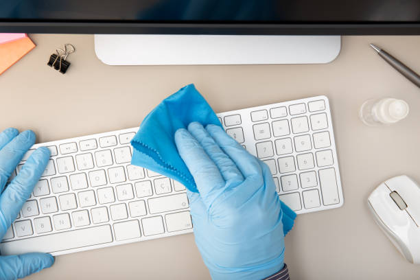 Hand with protective glove cleaning a keyboard with disinfectant Hand with protective glove cleaning a keyboard with disinfectant. COVID-19 Coronavirus outbreak prevention concept. Top view clean desk stock pictures, royalty-free photos & images