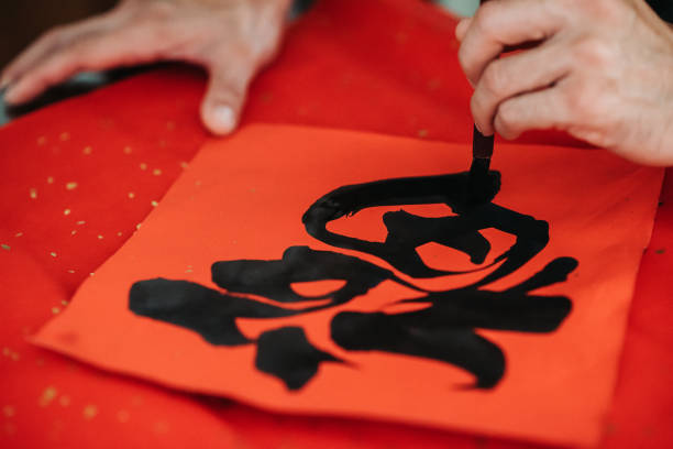 close up of hands writing chinese calligraphy characters with black ink on red colour paper
