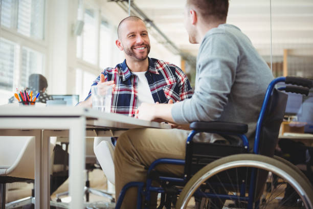 Handicap businessman sitting with colleague in office Handicap businessman discussing while sitting with colleague in creative office wheelchair stock pictures, royalty-free photos & images