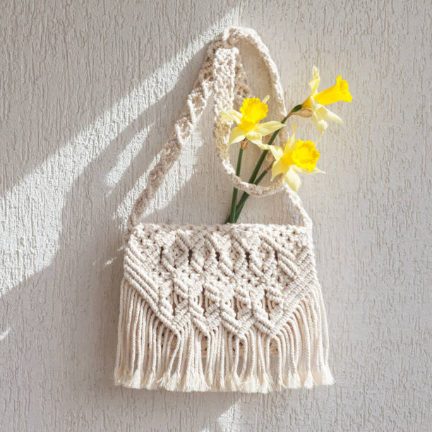 Handmade macrame bag with flowers on the light wall. ECO friendly natural macrame cotton bag. Hobby knitting handmade macrame. Modern summer concept. Copy space stock photo