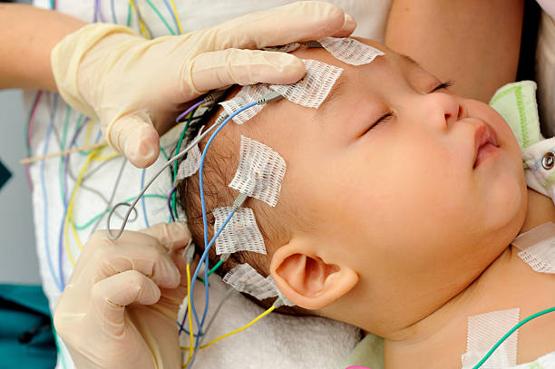 Hands applying electrodes to baby for electroencephalography Actual Electroencephalography (EEG) recording net being used on a baby. EEG is the recording of the brain's spontaneous electrical activity over a short period of time. electrode stock pictures, royalty-free photos & images