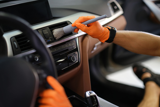 Male hands brush dust from the ventilation system in the car, close-up. Car interior, professional car cleaning service