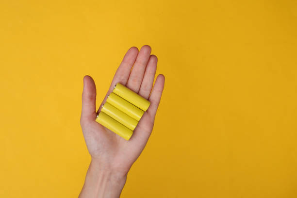Hands holding aa type battery on yellow background stock photo