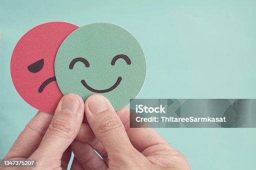 istock Hands holding sad face hiding behind happy face, bipolar and depression, mental health, split personality,  mood change, 1347375207