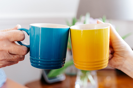 Close up image depicting two people doing a 'cheers' gesture with two coffee mugs. One mug is blue and the other is yellow - the colours of the Ukrainian flag.