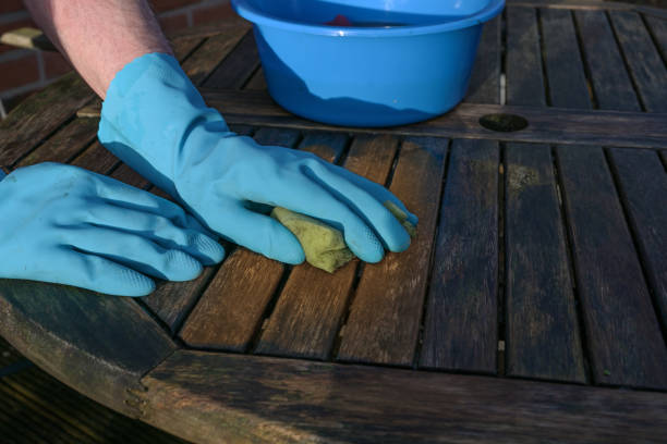 Hands in blue rubber gloves cleaning a weathered wooden garden table at the beginning of spring orthe outdoor season, copy space stock photo
