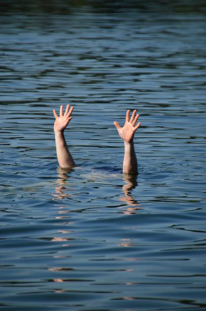 hands of a drowning person raised out of the water for help stock photo