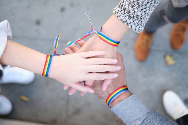 Hands of a group of three people with LGBT flag bracelets stock photo
