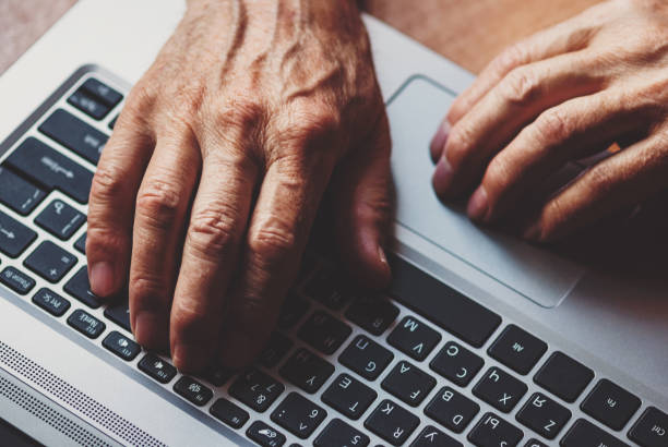 hands of a senior man typing on a laptop keyboard, learning to use computer in old age stock photo