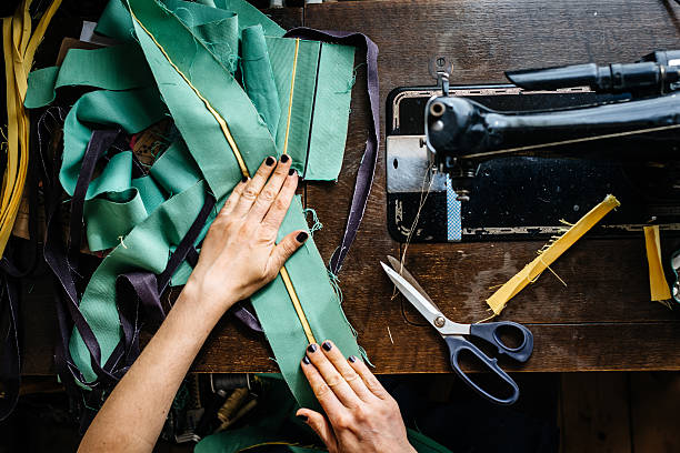 Hands of a woman sewing fabrics Overhead shot of hands of young female fashion designer with fabrics and scissor and an old sewing machine. tailor stock pictures, royalty-free photos & images