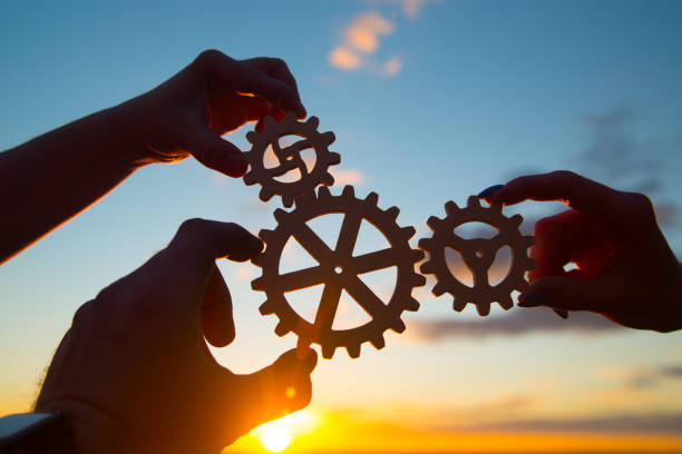 hands of businessmen assemble a puzzle from gears against the sky in the sunset. stock photo