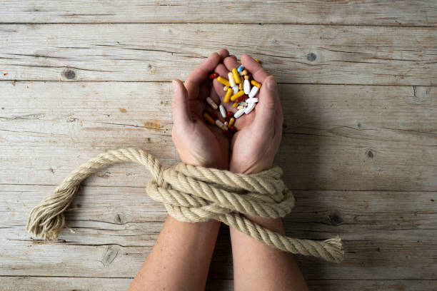 Hands of man are tied with a rope and in his hands he holds many different pills, concept addiction, drug addiction stock photo