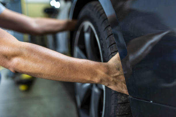 Hands of mechanic changing a wheel of a modern car Photo of a young Unrecognizable auto mechanic in uniform is examining a tire while working in auto service. Mechanic Holding Car Tire At Garage. cycle vehicle stock pictures, royalty-free photos & images