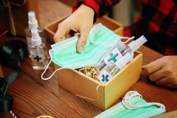 Hands of person collect gift during quarantine in a box. Hands of person collect gift during quarantine in a box. Surprise of antiseptics and medical masks on wooden table. face mask stock pictures, royalty-free photos & images