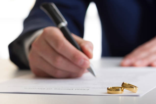 Hands of wife, husband signing decree of divorce, dissolution, canceling marriage, legal separation documents, filing divorce papers or premarital agreement prepared by lawyer. Wedding ring stock photo
