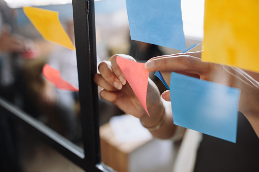 Close-up of hands sticking a sticky note onto a glass surface.