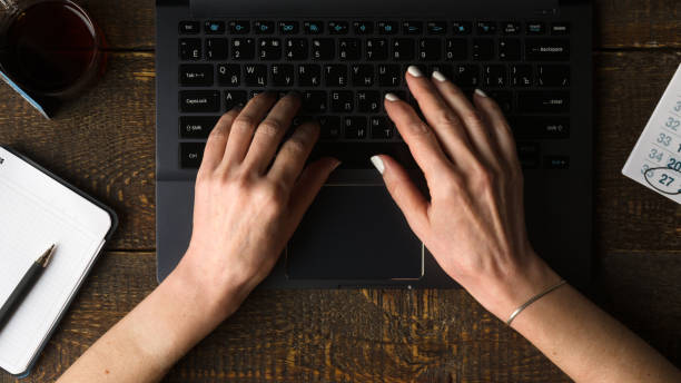 コンピューターのキーボードとノートとペンの手を上から表示します。 ストックフォト