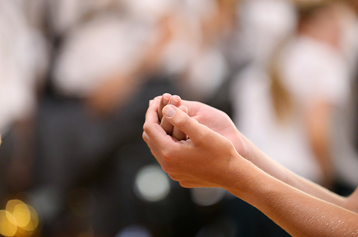 Close up image of a parishoners hands clasped receiving the bread during holy communion from a catholic priest at Mass.