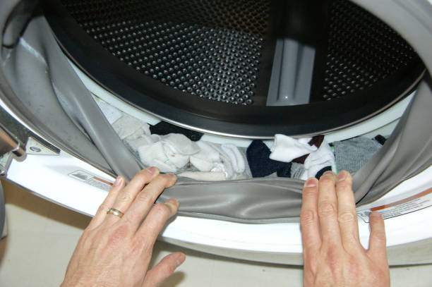 Hands pulling back the rim of washing machine drum to discover missing socks stock photo