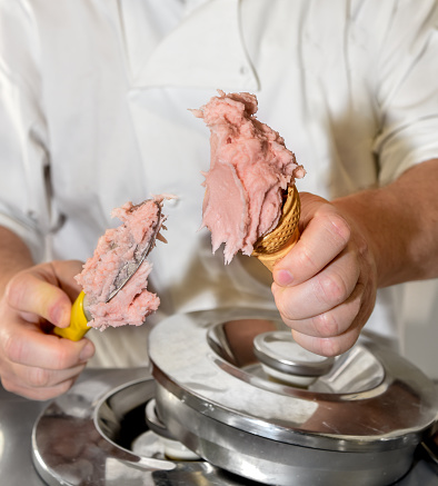 Hands of the ice cream man scooping strawberry ice cream into the waffle cone