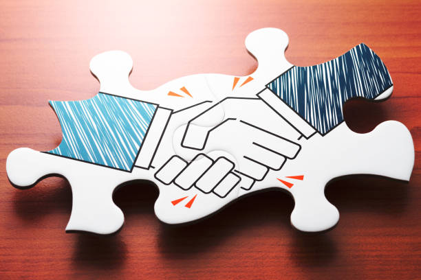 Handshake jigsaw puzzle pieces on wood desk. Concept image of agreement and partnership. coalition stock pictures, royalty-free photos & images