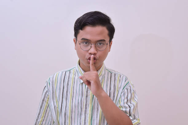 handsome Asian man making shushing gesture, asking to be quiet Portrait of handsome Asian man in casual stripe shirt with glasses making shushing gesture, asking to be quiet, silence concept. Isolated image on gray background how do you say shut up in japanese stock pictures, royalty-free photos & images