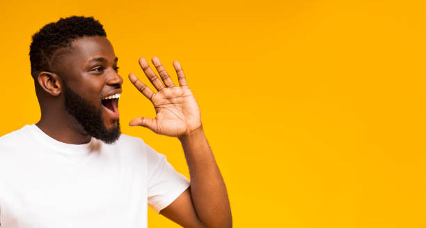 Handsome black man shouting at copy space, making announcement Attractive african guy shouting at copy space, making announcement, sharing news on yellow studio background. Panorama mouth open stock pictures, royalty-free photos & images