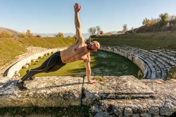 Handsome Body builder Man does phisical exercises outdoor. Innovative Gym in an ancient Roman amphitheater stock photo