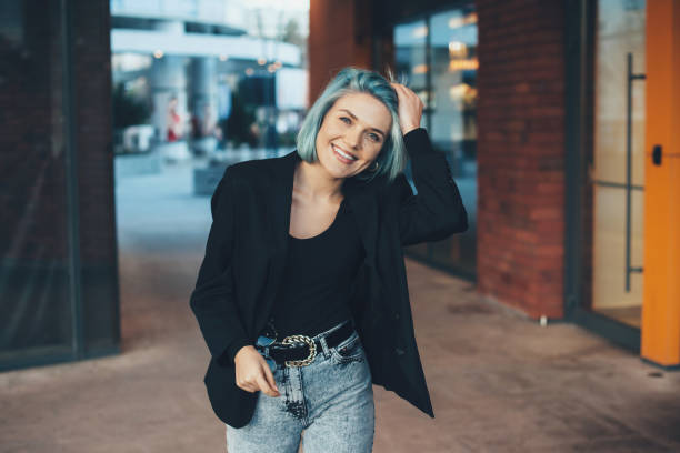Handsome caucasian woman with blue hair posing outside and touching her hair while smile at camera stock photo