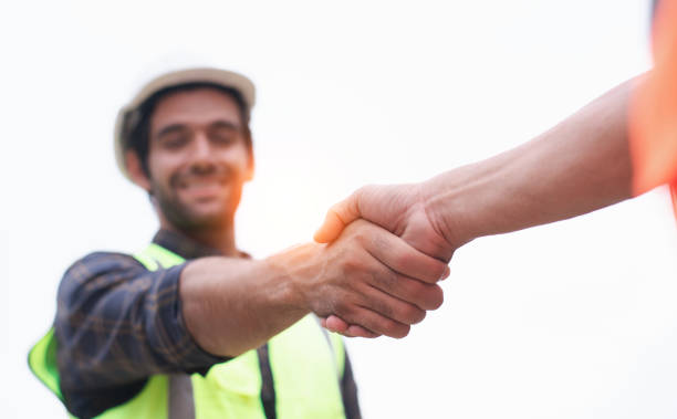Handsome construction engineer in protective helmets and vests are shaking hands while working in the office center stock photo