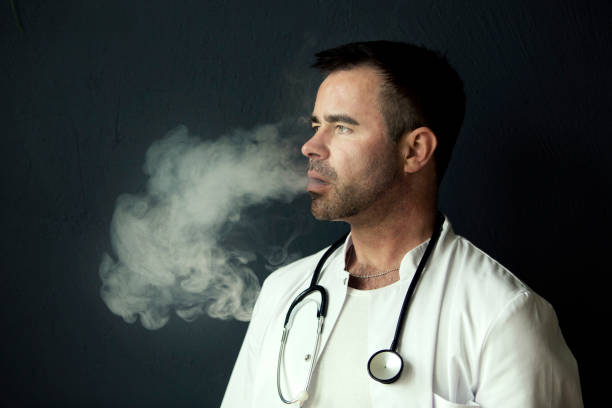 handsome doctor smoking and blowing out smoke portrait of handsome doctor smoking and blowing out smoke doctors smoking stock pictures, royalty-free photos & images