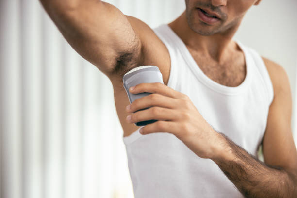 Handsome guy in t-shirt using deodorant in room Young male applying deodorant to armpit at his apartment stock photo deodorant stock pictures, royalty-free photos & images