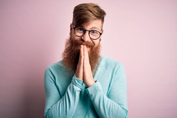 Handsome Irish redhead man with beard wearing glasses over pink isolated background praying with hands together asking for forgiveness smiling confident.  prayer request stock pictures, royalty-free photos & images