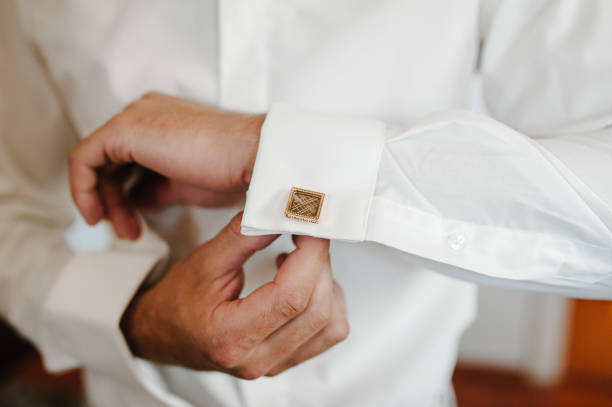 Handsome man buttoning cufflinks on white shirt. Groom's elegant male gold cufflink. wedding preparation morning of the groom. stock photo