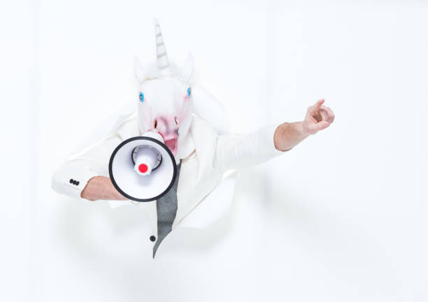 Handsome man in white suit wearing a unicorn mask  and holding a megaphone Handsome man horse mask photos stock pictures, royalty-free photos & images