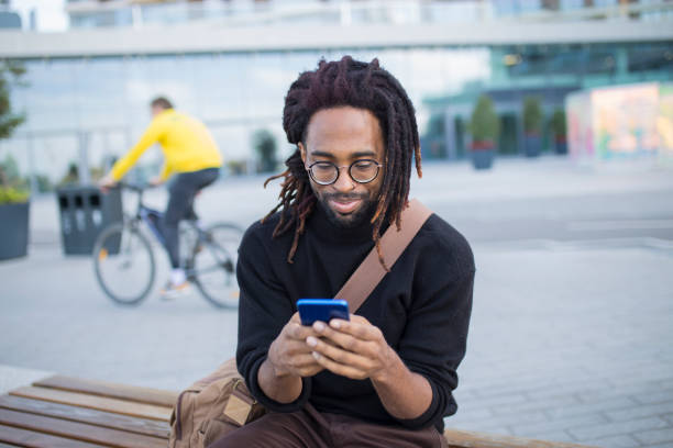 bir cep telefonu ile bir bankta oturan yakışıklı adam - hipster kişi stok fotoğraflar ve resimler