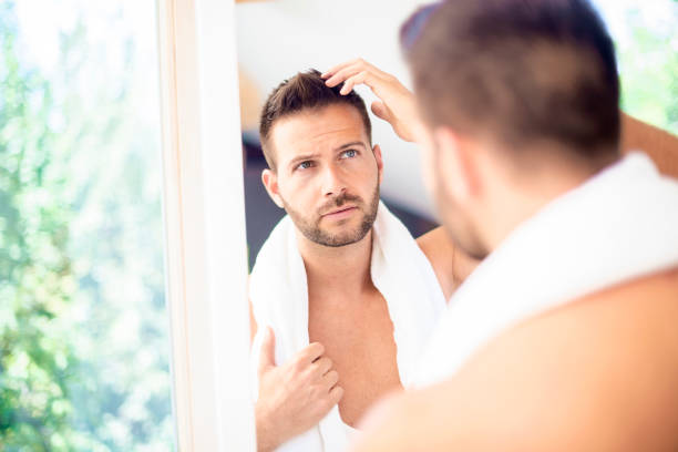 Handsome man standing in front of bathroom mirror and looking his face stock photo