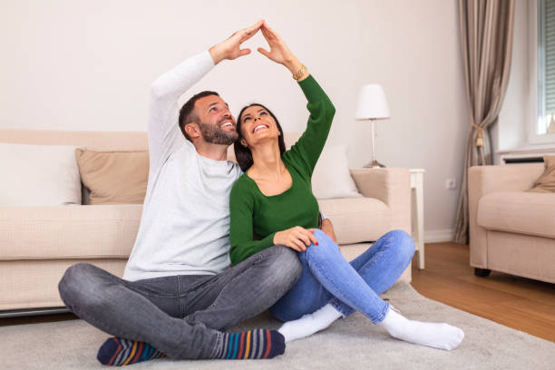 Handsome man with beautiful woman dreaming a new home. Happy married couple moves to new apartment. Happy couple making roof with hands symbol of new home and insurance protection plan. stock photo