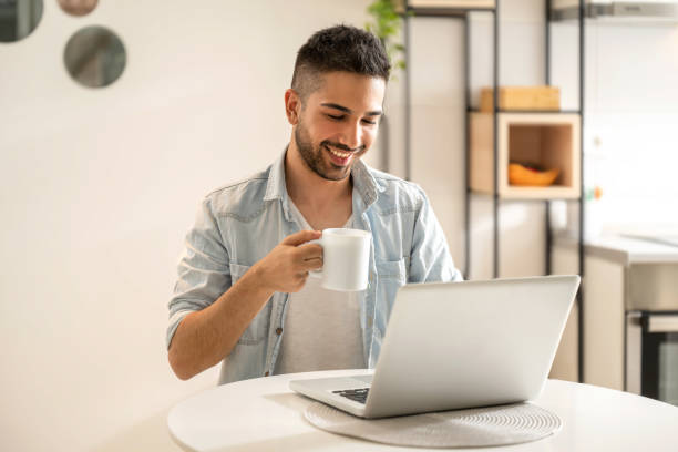 Handsome man working using computer laptop and drinking a cup of coffee at home office stock photo