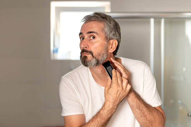 Handsome Mature Bearded Man Trimming His Beard Handsome Mature Bearded Man Trimming His Beard With a Trimmer at Morning in the Bath Room. Beauty, Hygiene, Shaving, Grooming and People Concept hedge clippers stock pictures, royalty-free photos & images