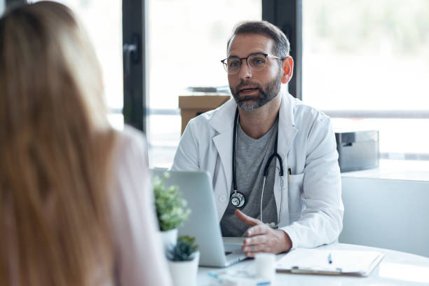 Handsome mature male doctor talking while explaining medical treatment to patient in the consultation. stock photo