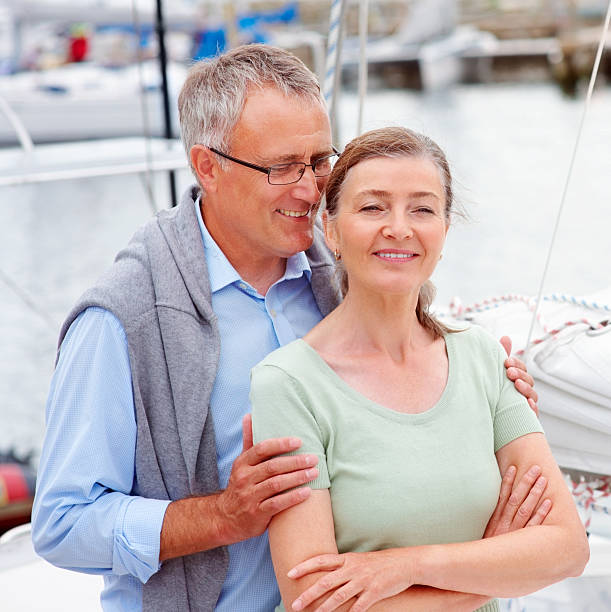 handsome old man whispering a secret into wife's ears on a sailboat - fluisterboot stockfoto's en -beelden