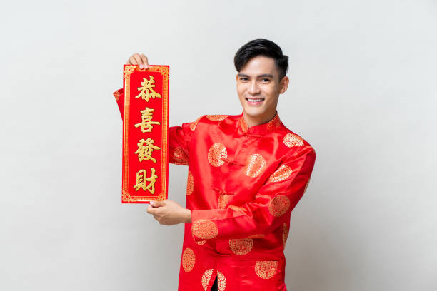 bello uomo asiatico sorridente che mostra un'etichetta rossa con testo significa che puoi ottenere una maggiore ricchezza in uno sfondo grigio chiaro da studio isolato per i concetti del capodanno cinese - blessin foto e immagini stock