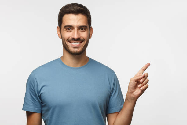 handsome smiling male in blue t-shirt pointing right with finger isolated on gray background - man pointing imagens e fotografias de stock