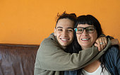istock handsome teenage boy hugging his mother affectionately and smiling at the camera while sitting on the sofa. Mother and son. family concept. 1366132035