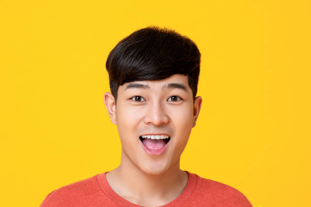 Handsome young Asian man face smiling with mouth open Studio portrait of  handsome young Asian man face smiling with mouth open isolated on colorful yellow background mouth open stock pictures, royalty-free photos & images