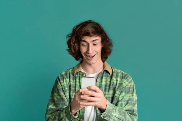 Handsome young guy communicating online via smartphone, color background Handsome young guy communicating online via smartphone, turquoise background cool blue world stock pictures, royalty-free photos & images