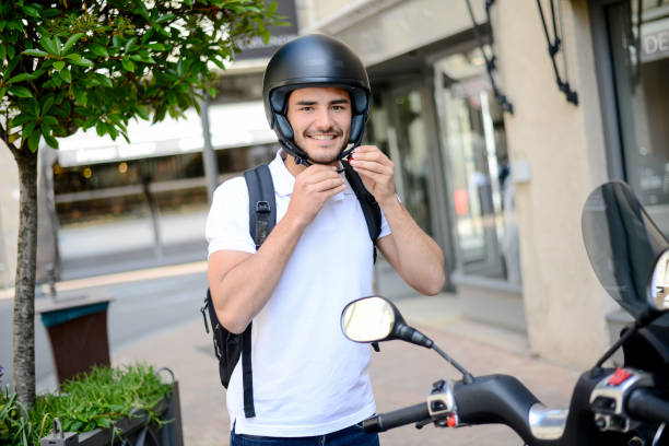 beau jeune homme dans une ville moderne, ajuster le casque de moto en été - casque moto photos et images de collection