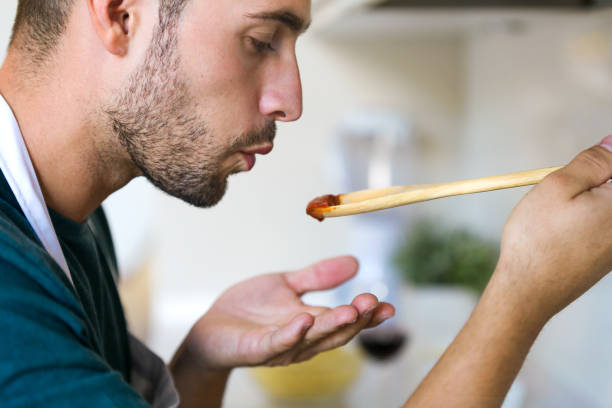 Handsome young man tasting the fried with wooden spoon in the kitchen at home. Close up of handsome young man tasting the fried with wooden spoon in the kitchen at home. tasting stock pictures, royalty-free photos & images