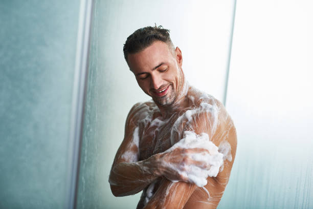 Handsome young man washing himself with shower gel stock photo
